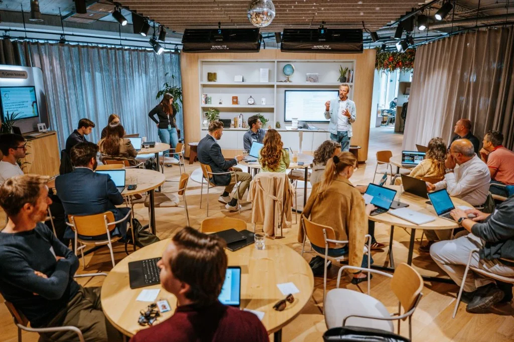 Live photo from the Friday September 25, 2026 Google AI Café Brussels workshop showing Jerome CG Paquay briefing the 5 Squad Tables under the disco ball